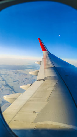 The wing of an airplane flying over clouds with a sunset sky. View from the airplane window.の写真素材