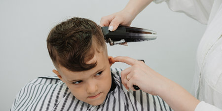 In the picture taken during the hair cutting process by a professional woman holding a special hair clipper in her hands, the child has dark hair.の写真素材