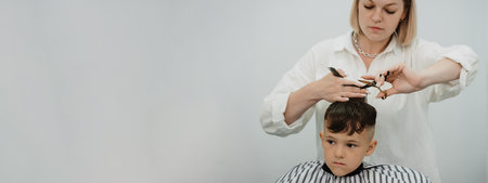 Boy in a barbershop getting a haircut from a female hairdresser. Stylists hands with tools. Childrens fashion in the salon.の写真素材