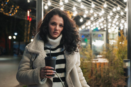A young brunette drinks coffee from a paper cup in a cold parkの写真素材