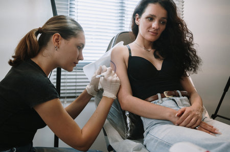 a professional female tattoo artist drawing a black tattoo on a womans arm by applying it with ink.の写真素材