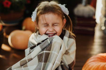 A cute Caucasian five-year-old girl is sitting on the porch of her house decorated with pumpkins and laughingの写真素材