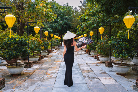 A woman in a traditional Vietnamese hat on the background of an Asian cultural garden decorated with...