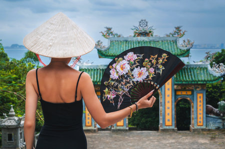 Woman traveler visiting at Linh Ung Pagoda temple. Tourist with Vietnamese hat and with a fan traveling in Da Nang city.の写真素材