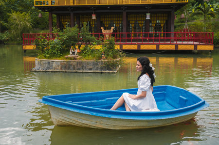 A young female traveler is sailing on a wooden boat on a lake against the background of a Buddhist temple standing on the water.の写真素材