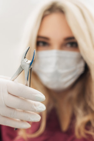 The dentist holds surgical pliers in her hands to remove a decaying tooth in the clinic