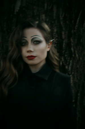 Portrait of a young woman in the Gothic gloomy image of a witch in the forest. Halloween costume. Vertical photo. Blur.の写真素材