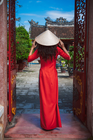 A tourist woman in a Vietnamese hat and a traditional dress on the background of a Buddhist temple