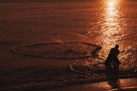 Silhouette of a fisherman fishing with nets in the sea at dawn.の写真素材