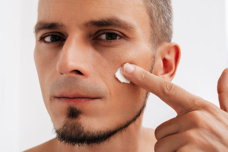 close-up of a man applying skincare cream to his cheekの写真素材