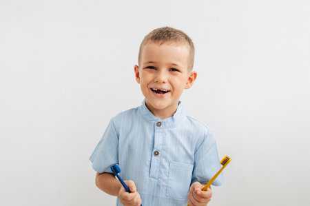 child holding yellow and blue toothbrushes, smiling with a missing baby toothの写真素材