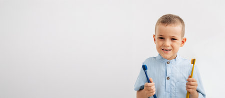 smiling boy with a natural baby tooth gap holding two colorful toothbrushes on a white backgroundの写真素材