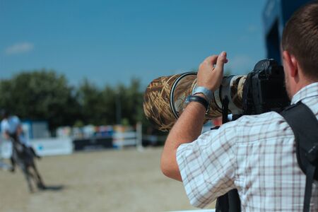 Huge zoom lens on a camera, photographer taking a picture by the zoom lens at a Show Jumping Competitions, camera lens in focusの写真素材