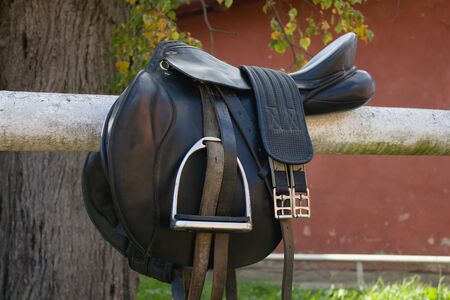 Black leather saddle on a barrier in the horse stableの写真素材