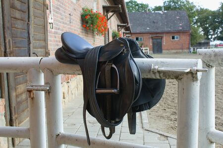 Black leather saddle on a barrier in the horse stableの写真素材