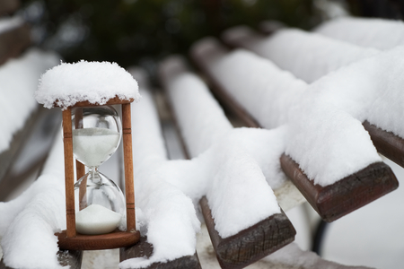 hourglass on a snow covered bench, white sandglass time passing at a winter seasonの写真素材
