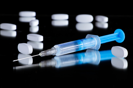 Medical syringe and pills on a black reflective surface, needle and drugsの写真素材