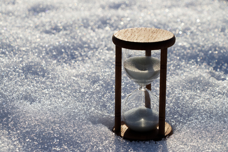 hourglass in the snow, white sandglass time passing in and backlitの写真素材