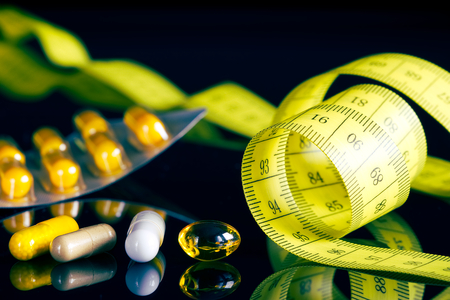 Medical pills for healthy diets, vitamin tablets as a dietary supplement, measuring tape as a symbol of slim, black backgroundの写真素材