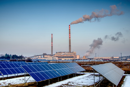 solar panels and coal power plant with smoking chimneys, ecological and outdated way of getting electricityの写真素材