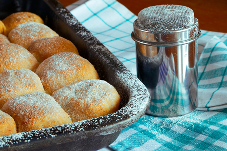 sugared poppy and plum buns on baking tray with sugar bowl, kitchen towels and wooden tableの写真素材