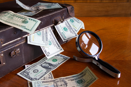 suitcase full of money on the table, magnifying glass as a symbol of financial investigations, scattered dollar billsの写真素材