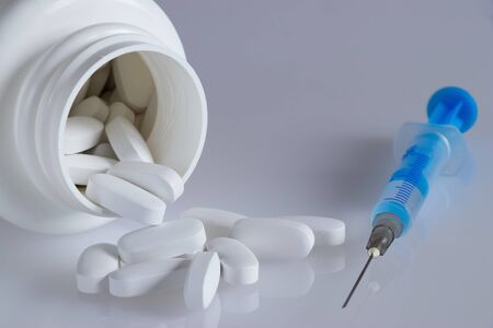 White plastic bottle with pills and medical syringe on a light gray background, spilled tablets, medical supplementsの写真素材