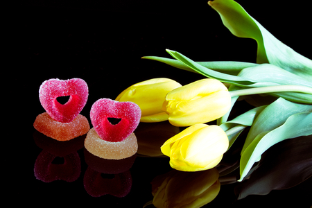 Romantic sugared sweets and a bouquet of yellow tulips, jelly candies with flowers as a gift on a black backgroundの写真素材