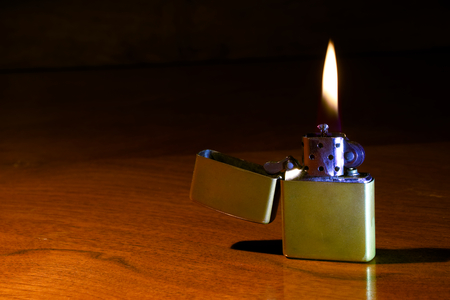brass gasoline lighter on the wooden table, Ignited and cigarette lighter, lighter flame on a dark backgroundの写真素材