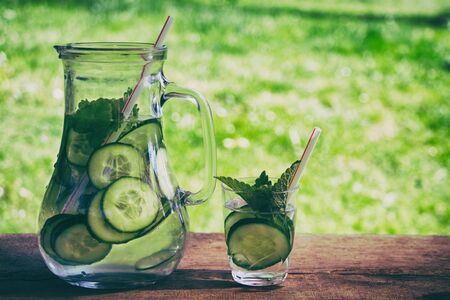 Refreshing summer detox drink in the garden. Fresh sliced cucumber with mint leaves in a glass of water.の写真素材