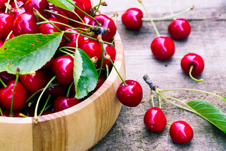 Red ripe cherries in a wooden bowl on an old wooden table. Several sprouted sweet cherries around. Close up view of cherries.の写真素材