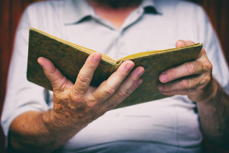 Senior man is reading old book. Pensioner is holding a book. Old man is relaxing with book.の写真素材