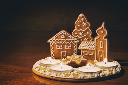 Homemade gingerbread house lit by candles on a dark background. Christmas dessert on the table. Ginger decoration.の写真素材