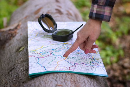 Hiking woman pointing to a tourist map where it is located and where to go. Travel concept with maps and compass. のeditorial素材