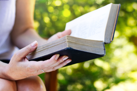 Woman is sitting in chair and reading a big old book. Relaxing in the garden with a book in hands. Read an old book in the garden.の写真素材