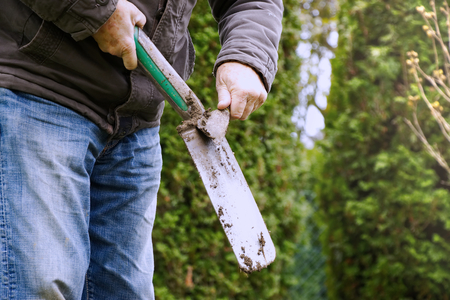 Gardener cleaning a spade from soil. Man using a big shovel for digging lawn. Gardening in spring.の写真素材