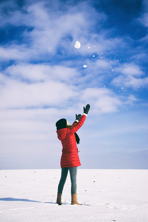 Happy woman is playing with snowball. Young woman enjoying from snow during a sunny day at winter season. Girl is wearing winter clothingの写真素材