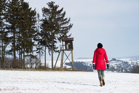 Hiking woman is walking to a hunting tower in countryside at winter season. Woman is wearing winter clothes on a walk in snowy natureの写真素材
