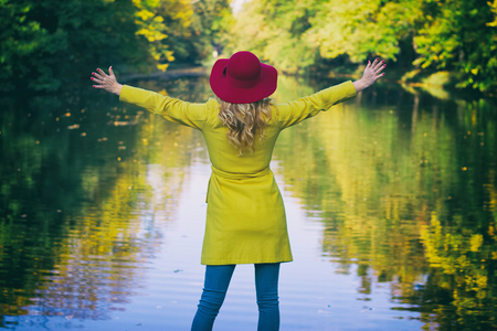 Fashion woman with red hat in park and enjoying view on a lake, autumn season. Trendy young girl wearing woolen coat. の写真素材