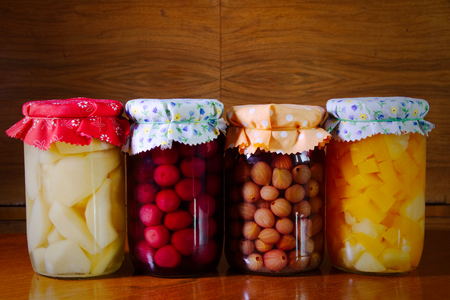 Homemade preserved fruit in jar, conserved fruit in glass on wooden table, organic food, stored homegrown cherries, gooseberries, pumpkins, pears.の写真素材