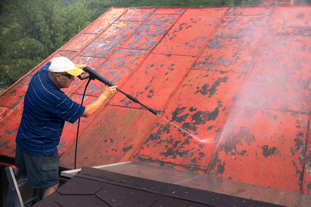 Man is washing the roof with a high pressure washer. Worker cleaning a red metal sheet roof by water.の写真素材