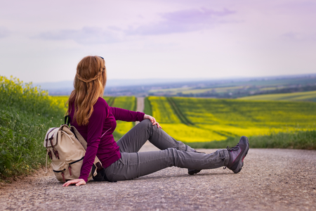 Woman sitting on a road in the middle of countryside. Traveler resting during trip. Travel concept. の写真素材