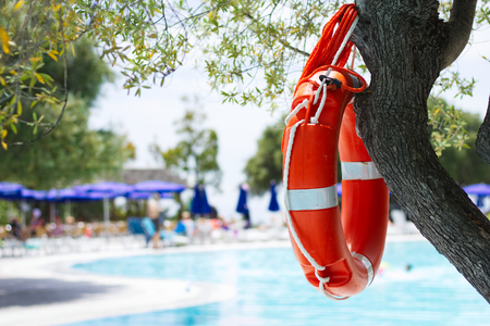 Lifebuoy by the pool at summer holiday resort, red lifesaver next to swimming poolの写真素材