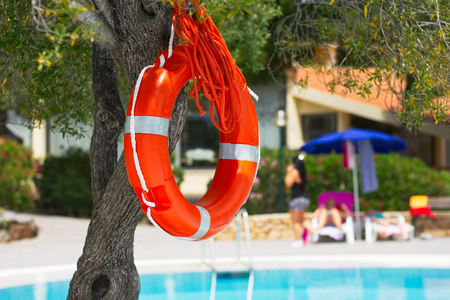 Lifebuoy by the pool at summer holiday resort, red lifesaver next to swimming poolの写真素材