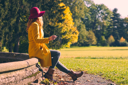 Fashionable woman sitting on old fountain and enjoying autumn season and smoking cigaretteの写真素材
