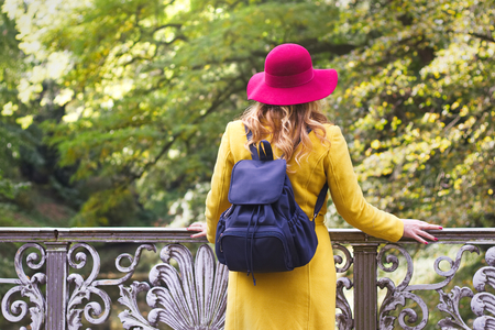 Beautiful woman is wearing woolen coat and red hat. Tourist woman standing on bridge in public park at autumnの写真素材