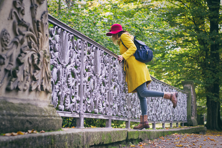 Beautiful woman is wearing woolen coat and red hat. Tourist woman standing on bridge in public park at autumnの写真素材