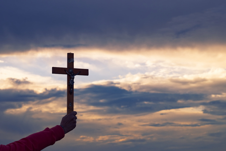 Hand holding christian cross, silhouette of crucifix on dramatic sky. Pray to Jesus Christ.の写真素材