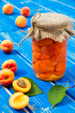 Homemade tasty apricot compote in glass jar and apricot fruit on blue wooden table. Preserved fruit and ripe apricot in harvest season.の写真素材