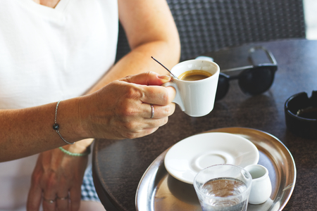 Woman drinking hot coffee in outdoor cafe, Woman sitting in restaurant and holding a cup of espressoの写真素材